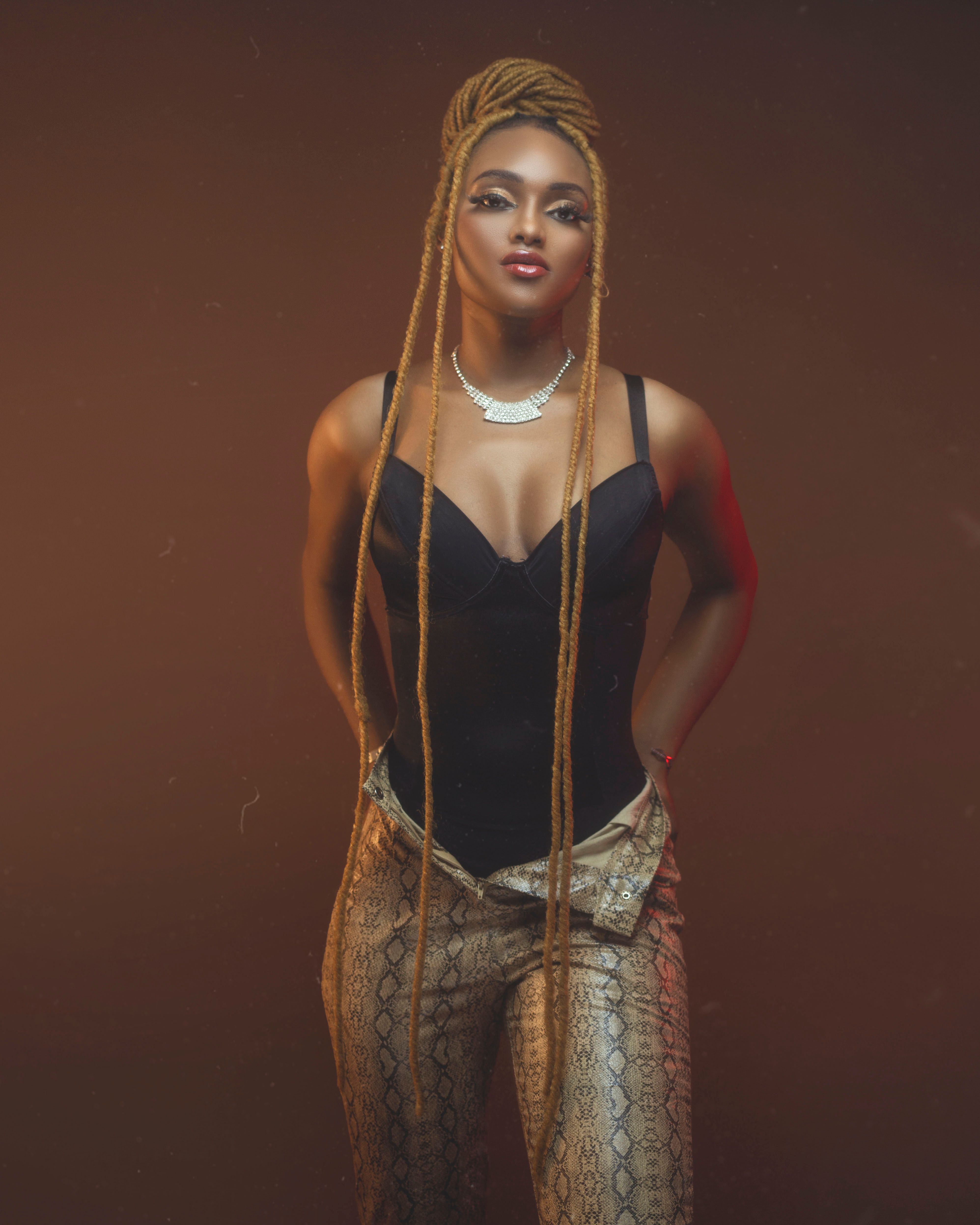 Studio portrait of a fashionable young African woman with long braids against a brown background.