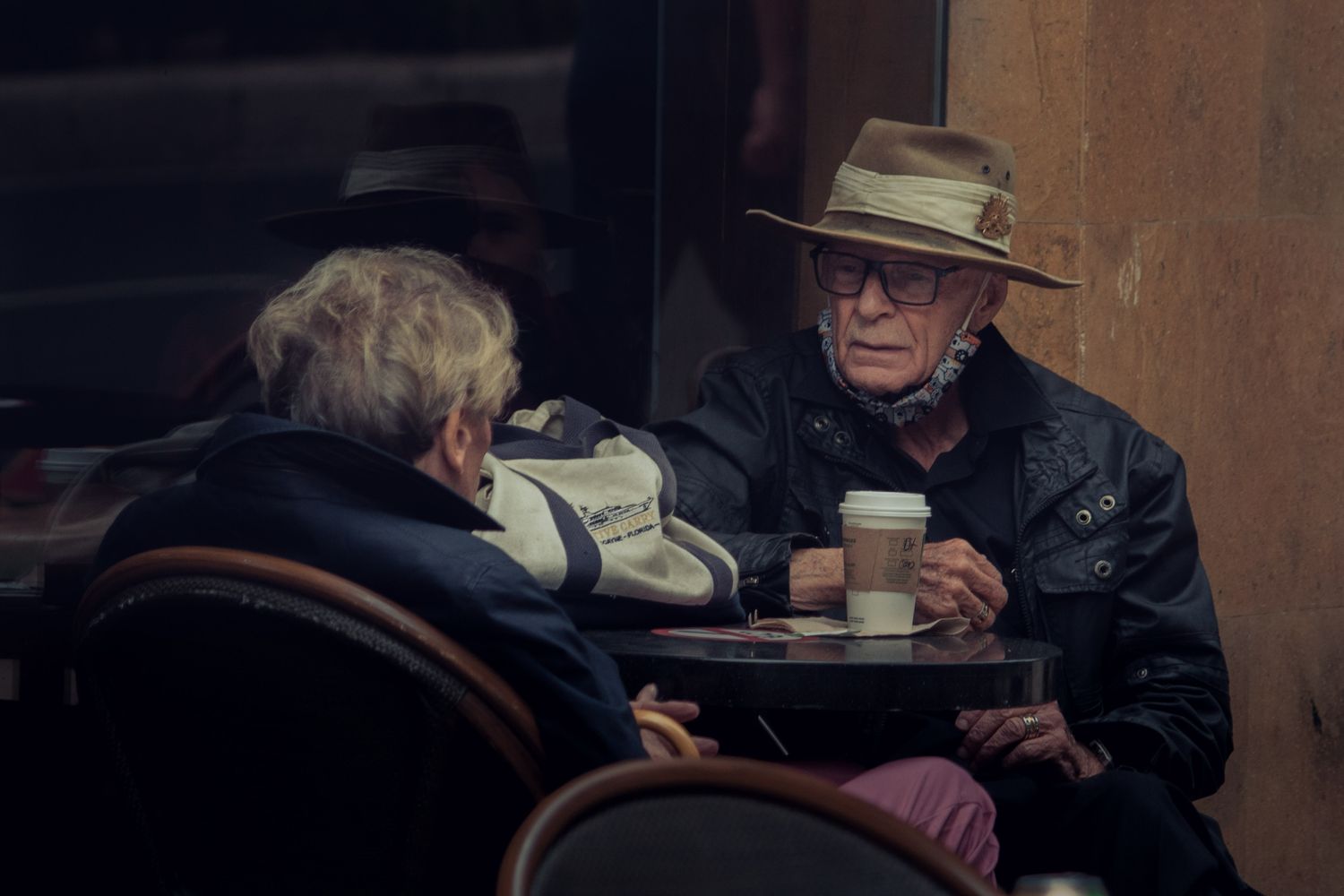 Un couple âgé et complice partageant un moment en terrasse, dans une lumière chaleureuse