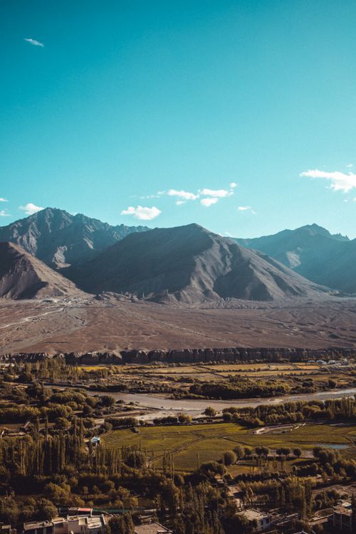 Free A breathtaking aerial perspective of a lush valley, surrounded by majestic mountains under a clear sky. Stock Photo