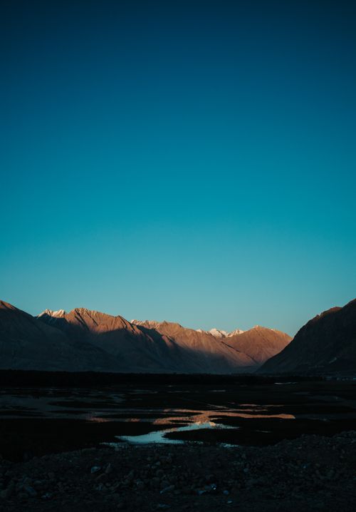 Free A tranquil mountain landscape with a blue sky and sunset glow, reflecting in a calm lake. Stock Photo