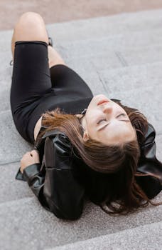 Caucasian woman in black leather jacket laying on stairs, embracing modern urban style.
