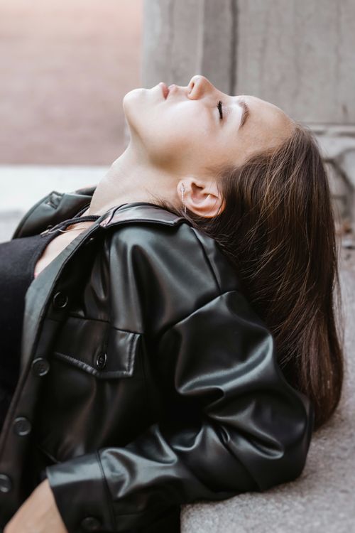 Free A young woman leans back in a leather jacket, gazing upwards in an outdoor setting. Stock Photo