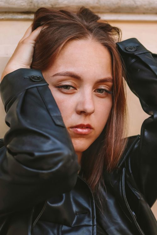 Free Close-up portrait of a woman posing with hands on head in a black leather jacket. Stock Photo