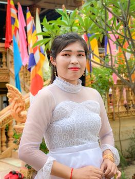Smiling woman in a white lace dress amidst vibrant cultural decorations outdoors.
