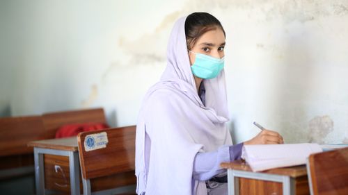 Free A young student in a hijab studies while wearing a face mask in a classroom. Stock Photo