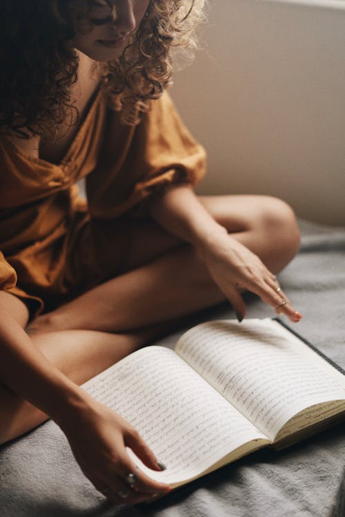 Woman Reading a Notebook on a Bed