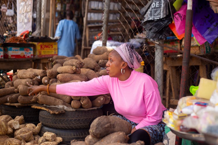 Woman In Pink Sweater Selling Root Crops In The Market