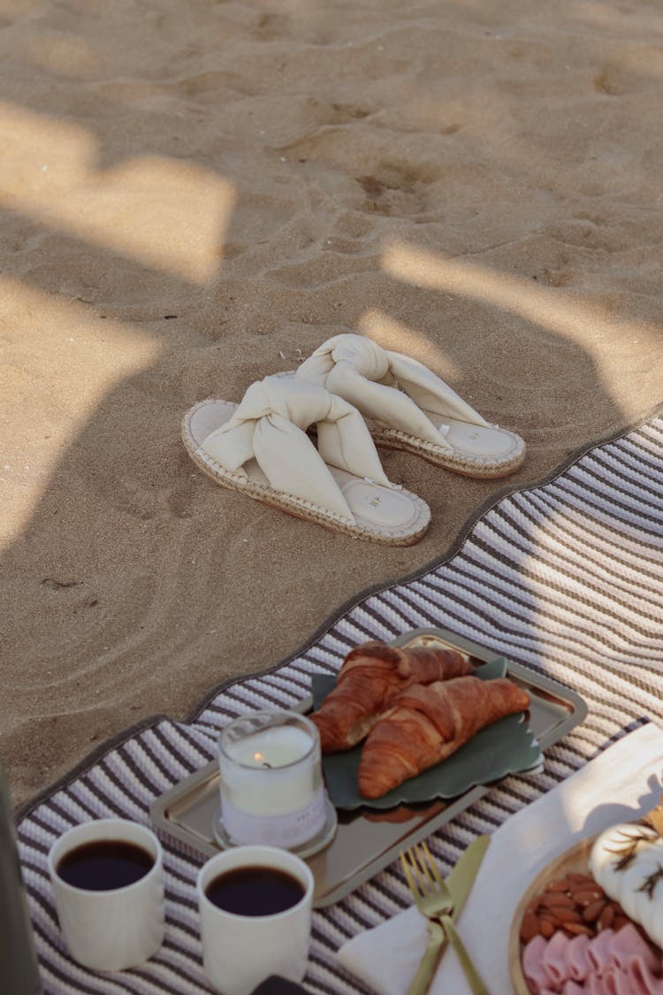 Sandals, Croissants And Coffee On A Towel On A Beach