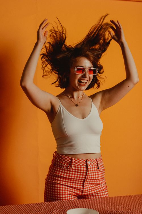 Free A happy woman celebrates with raised hands, wearing checkered pants and sunglasses. Stock Photo