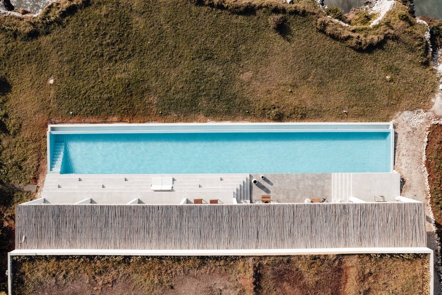 Aerial view of the long infinity pool and pavilion roof on the grassy bluff