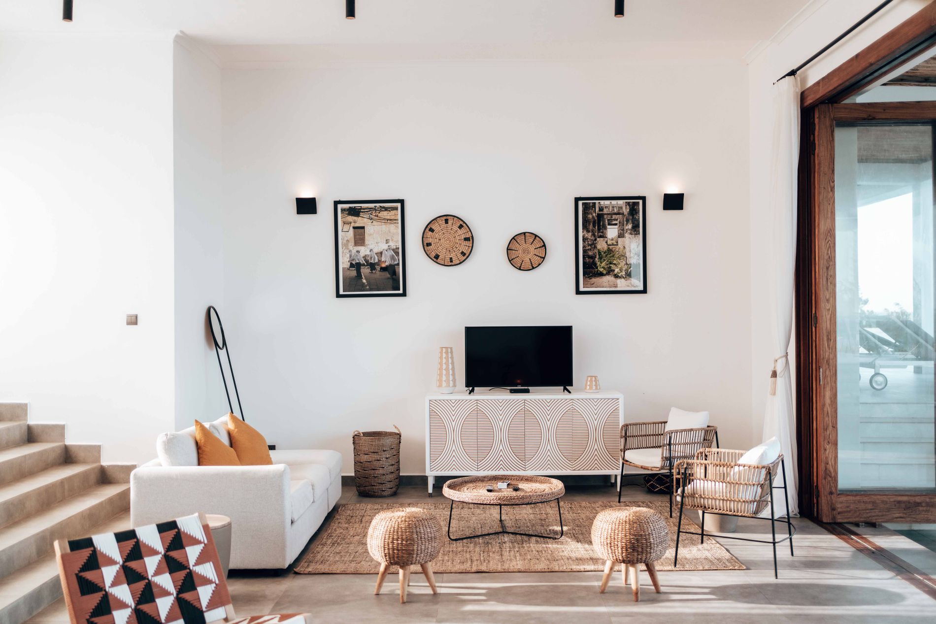 Bright contemporary living room with wicker seating, a neutral sofa, wood furniture, woven accents, and indoor greenery