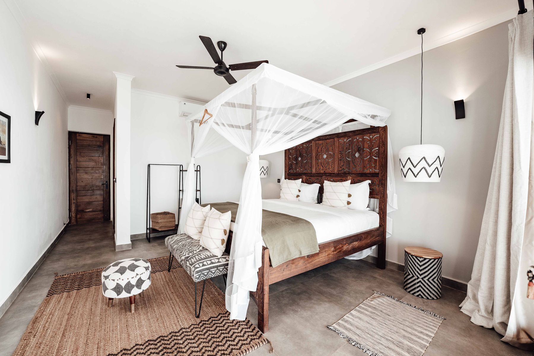 Dark carved four-poster bed with pale bedding in a bright neutral bedroom