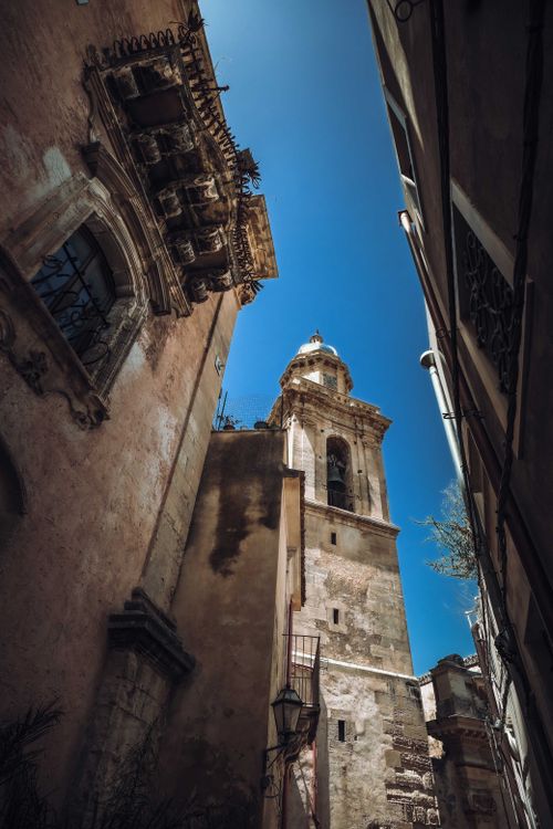 Free Low-angle view of a historic cathedral's steeple against a clear blue sky framed by surrounding buildings. Stock Photo
