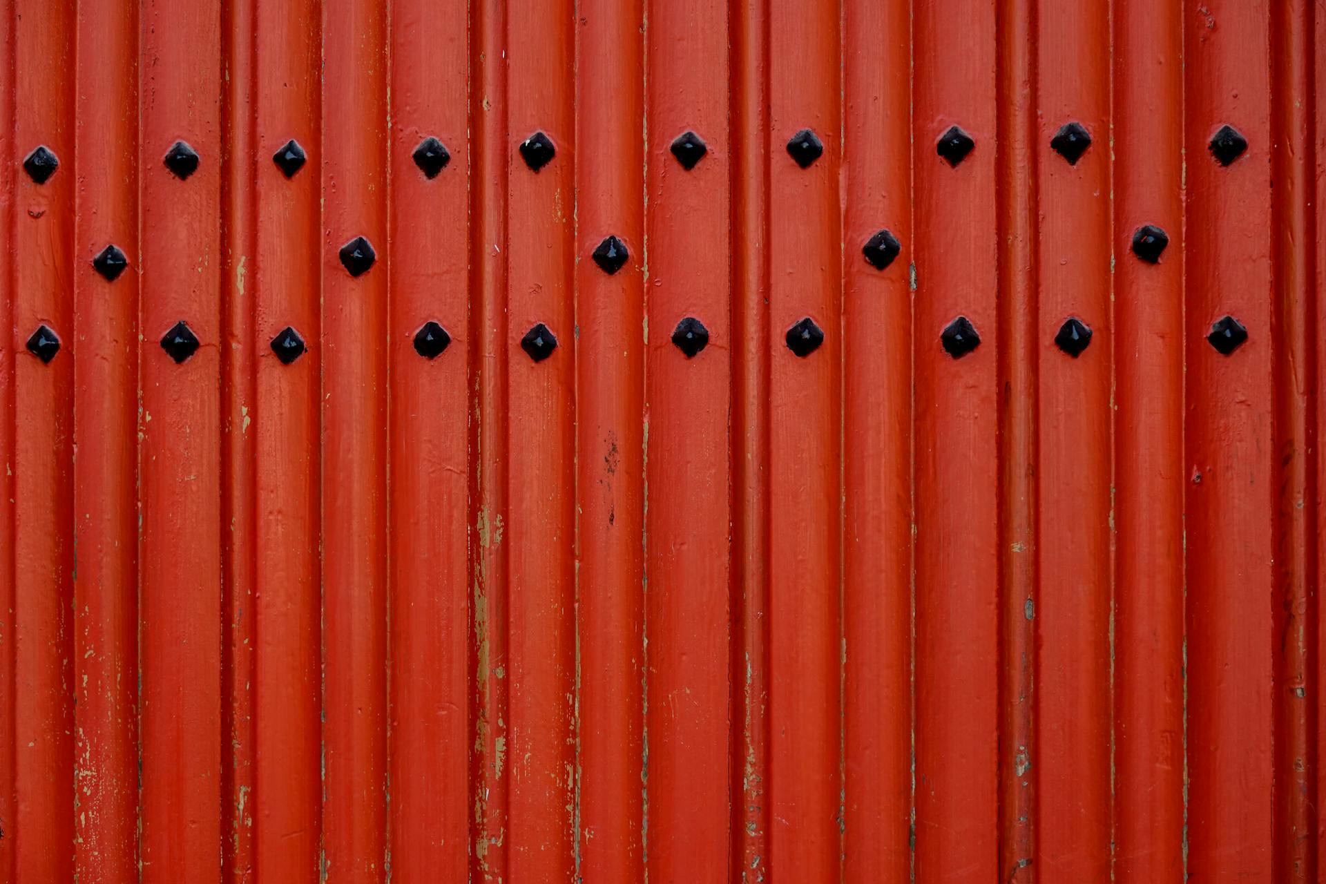Close-up of a red corrugated metal wall with black decorative studs.