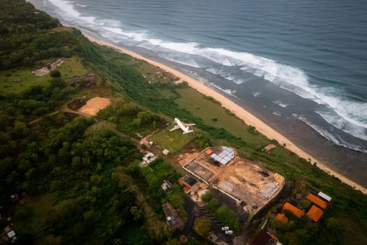 Drone shot of a construction site and airplane near Bali's scenic shoreline.