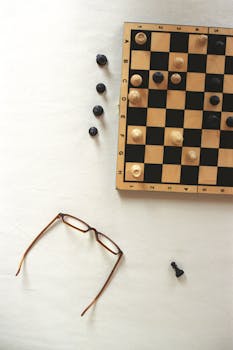 Chessboard with pieces and eyeglasses on a white surface, representing strategy.