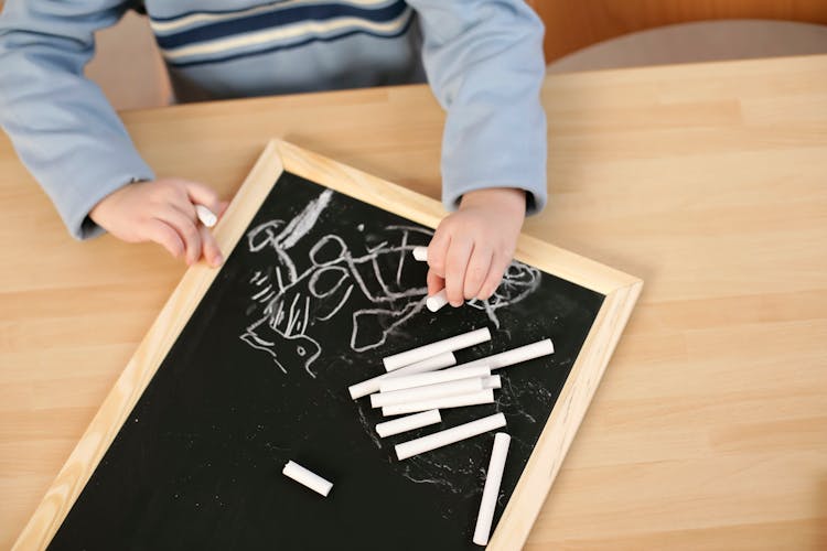 A Kid Writing With Chalk Over A Blackboard