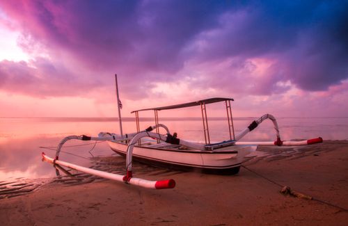 Free Traditional boat rests on a tranquil beach at sunrise with vibrant sky colors. Stock Photo