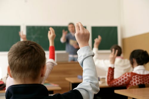 Photo of a Pupils Sitting in a Classroom with Raised Hands