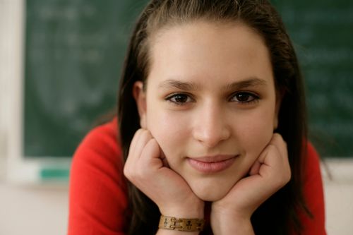 Free Close-up portrait of a brunette woman posing with hands on cheeks in a classroom. Stock Photo