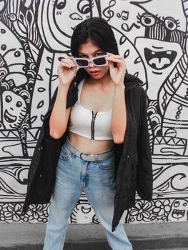 Fashion-forward Asian woman posing against vibrant street art in Davao, Philippines.