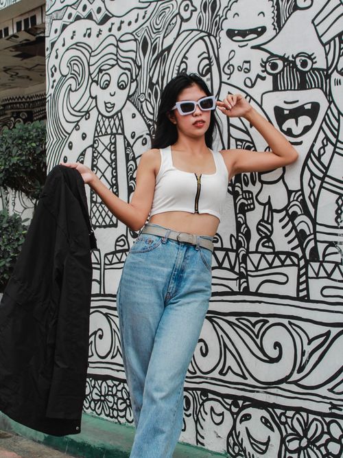 Free Young woman posing in trendy outfit against a vibrant mural wall. Stock Photo
