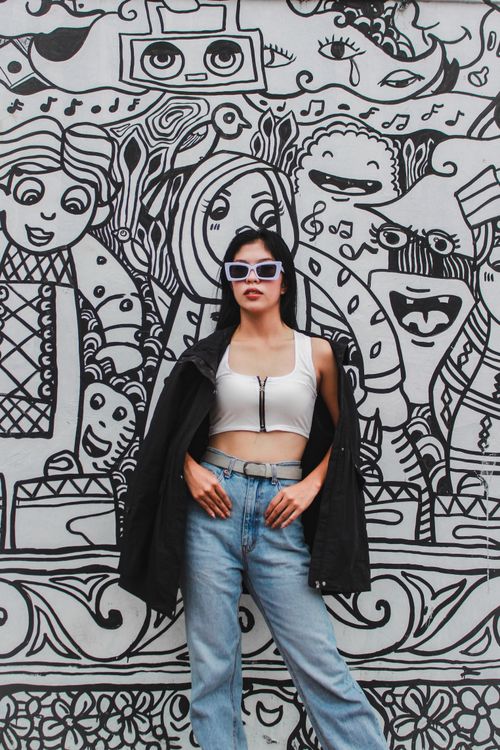 Free Fashion-forward woman poses in front of an artistic graffiti wall, displaying modern style. Stock Photo