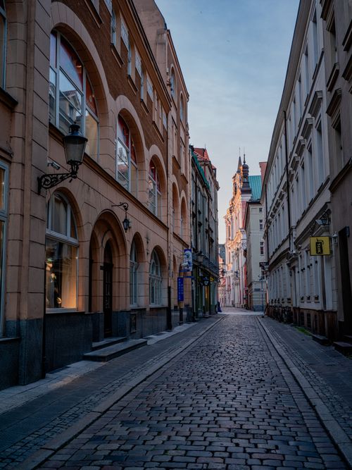Free Narrow cobblestone street lined with historic buildings at sunset, showcasing European architecture. Stock Photo