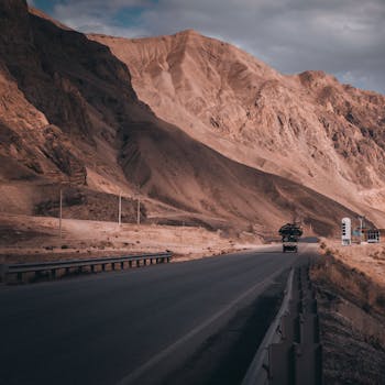 Remote highway cuts through dramatic, arid mountain landscape under cloudy skies.