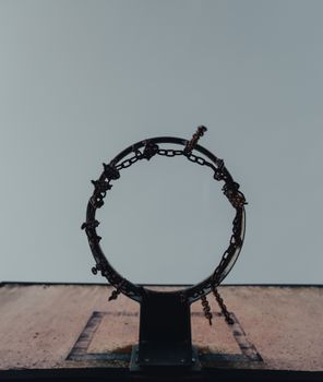 A low angle view of a rustic basketball hoop with chains, set against a gray sky, creating a dramatic scene.