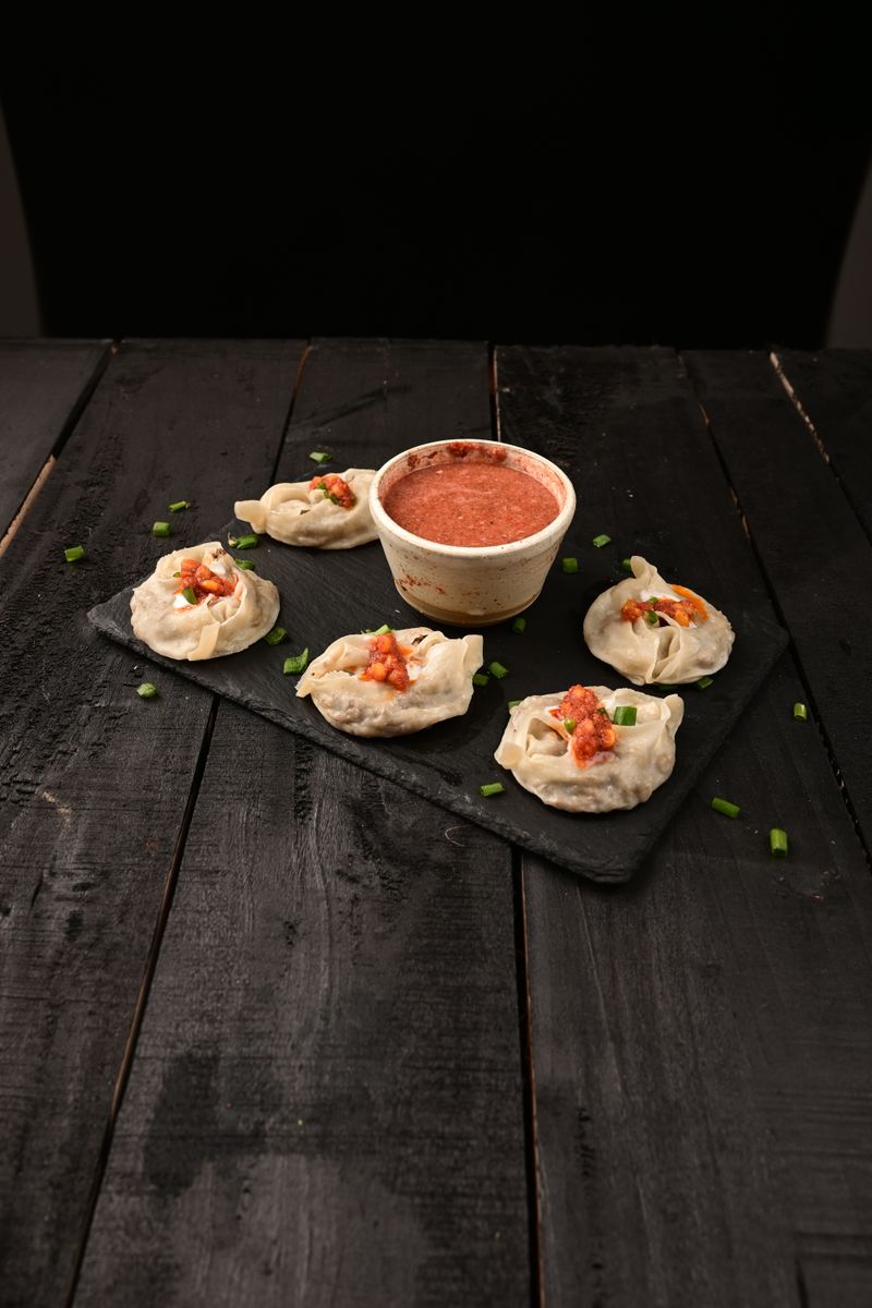 Savor the taste of Afghan mantu dumplings served with a spicy tomato sauce on a rustic surface.