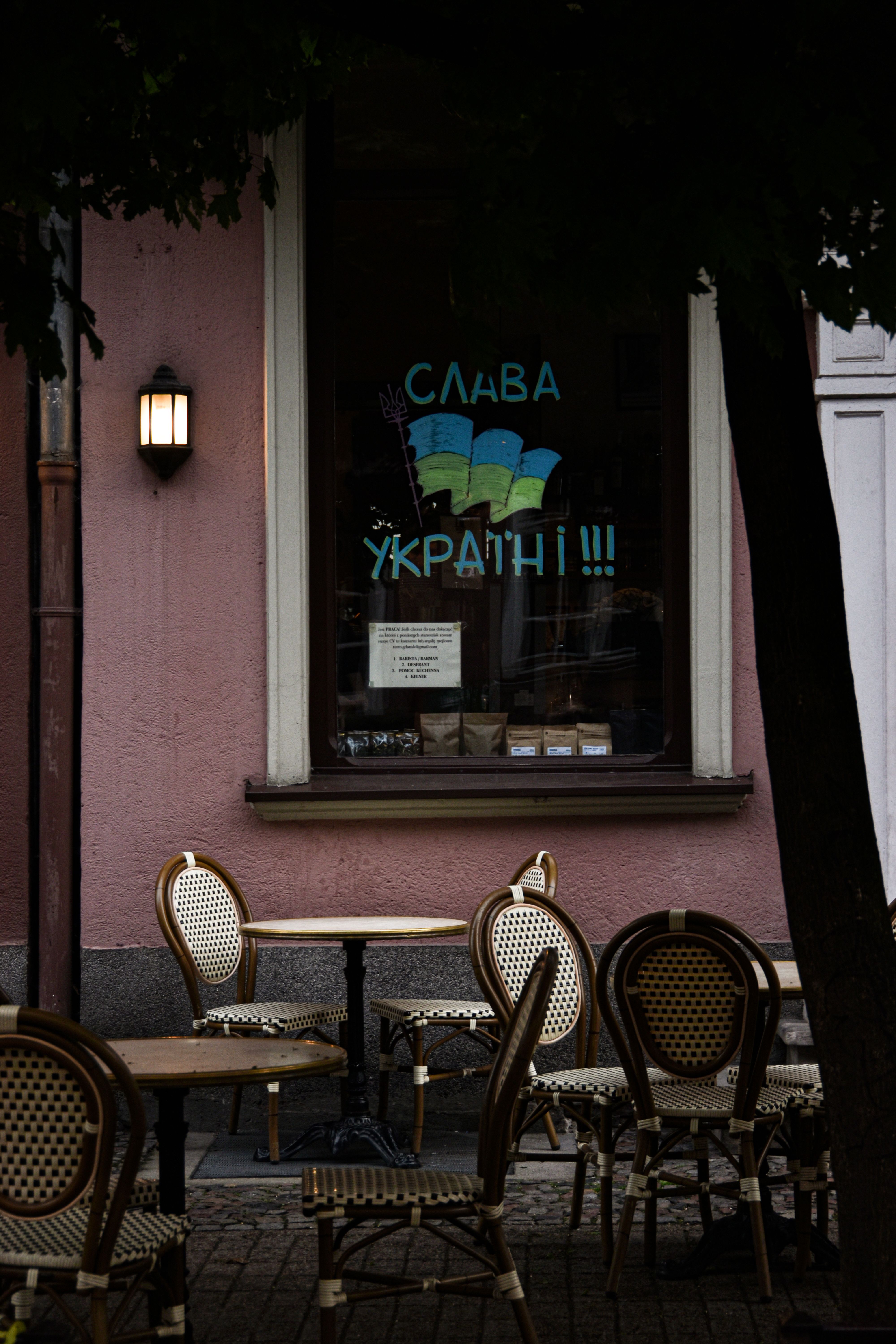 Outdoor café with chairs and tables, featuring Ukrainian slogan on the window, ambient street setting.