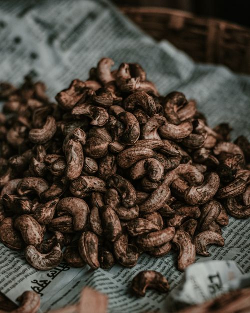 Free A close-up of raw cashew nuts scattered on a newspaper surface, displaying texture and detail. Stock Photo