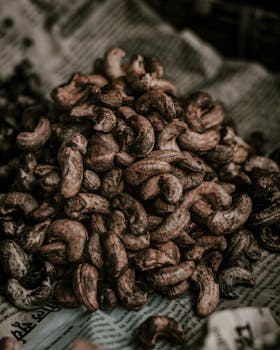Close-up of a pile of unpeeled cashews displayed on newspaper.