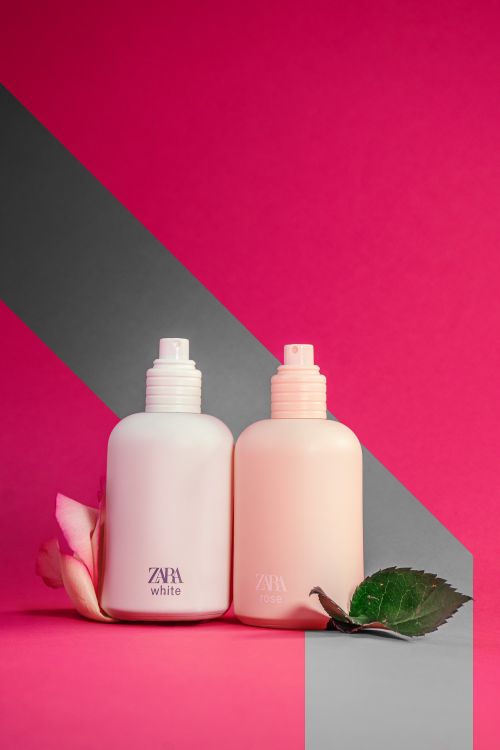 Free Stylish product shot of fragrance spray bottles with floral elements on a pink and gray backdrop. Stock Photo