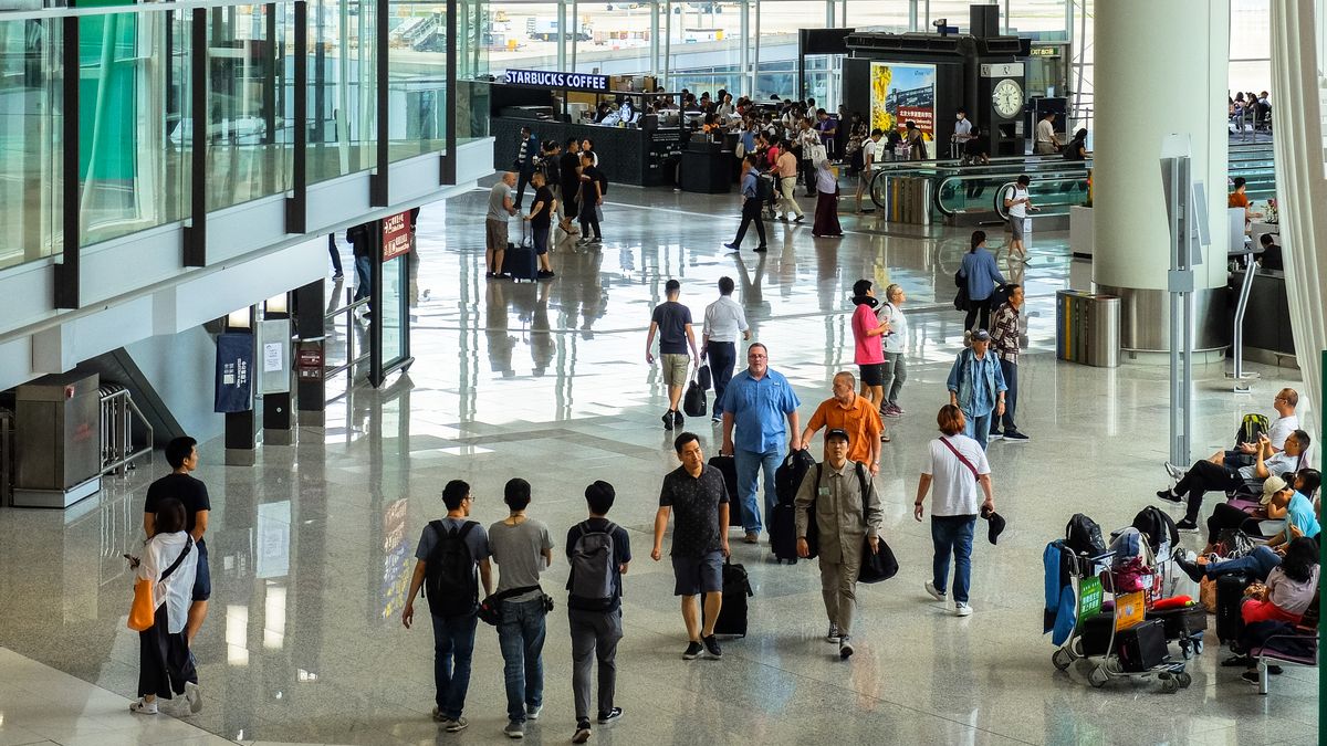 Passengers walking and seated in a bustling Hong Kong airport terminal.