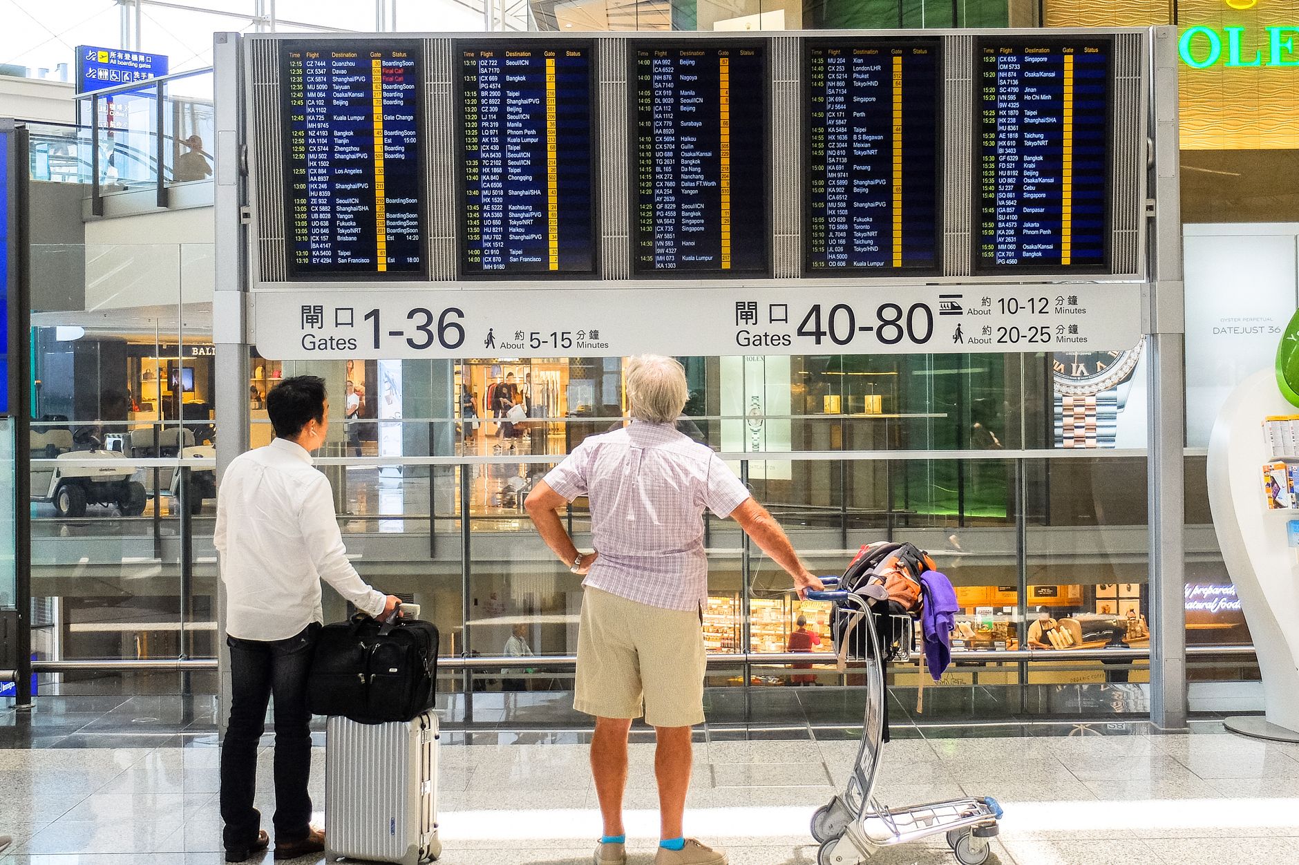 Passengers checking a departure board while route changes ripple through an airport terminal.