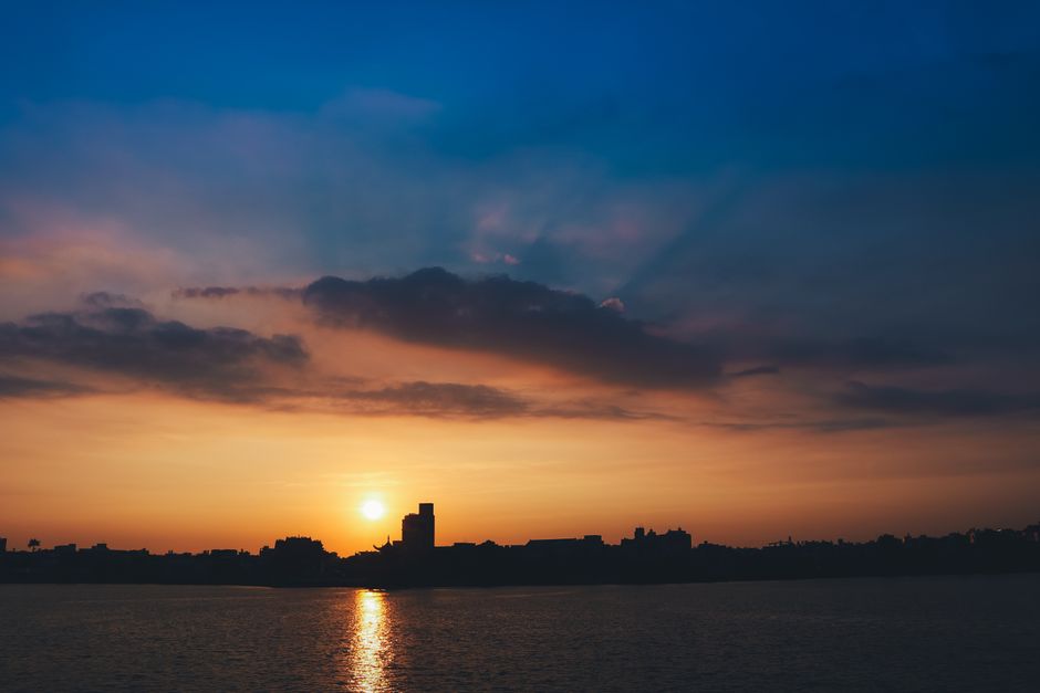 Peaceful sunset with city silhouette and ocean reflection, creating a tranquil seascape view.