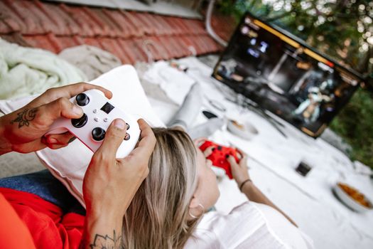 A couple playing video games outdoors, focusing on the controllers and screen.