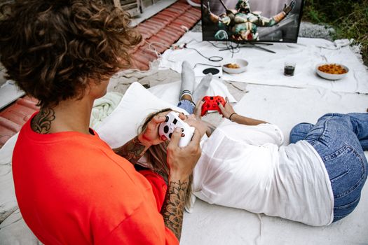 A couple relaxes outdoors playing video games together on a console.