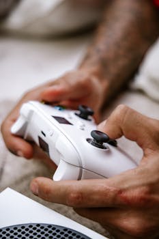 Hands gripping a white gaming controller with a blurred background, showcasing a focus on gaming.
