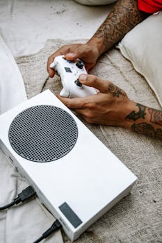 Close-up of tattooed hands holding a game controller with a white console, perfect for tech and gaming themes.