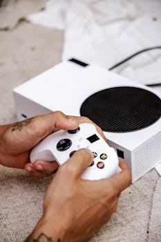 Close-up of hands holding a game controller connected to a white gaming console indoors.