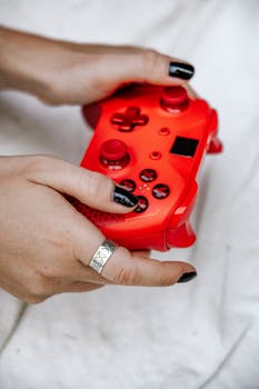 Detailed shot of hands holding a vibrant red game controller with black buttons.