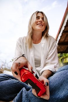 A joyful woman playing video games outdoors with a vibrant red controller, capturing a relaxed and fun moment.