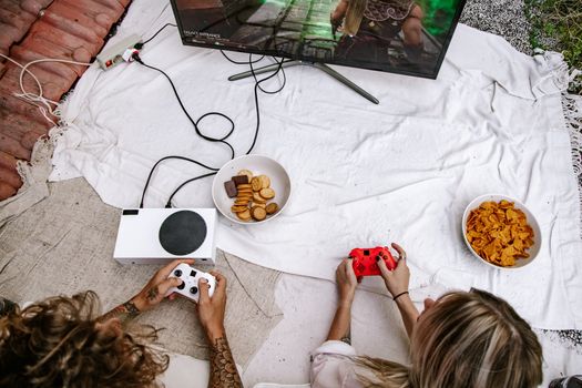 Top view of a couple gaming outdoors on a console with snacks setup on a white sheet.