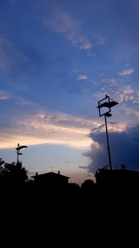 Street lamps silhouetted against a dramatic evening sky with clouds in Italia.