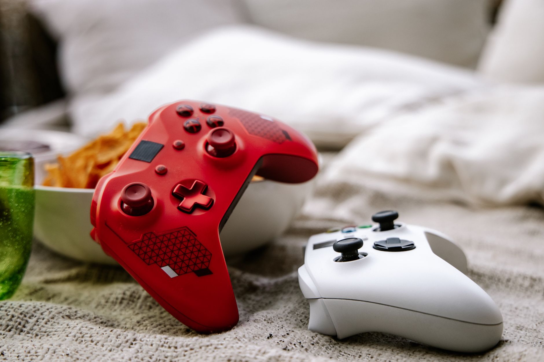 A red and white Xbox game controllers placed on a cozy blanket next to snacks. Perfect for gaming themes.