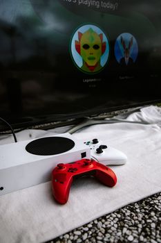 Close-up of a white gaming console with a vibrant red controller in front of a TV screen displaying avatars.