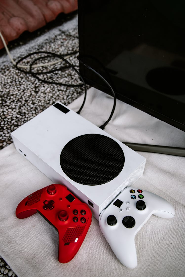 Xbox Console And Wireless Controllers On A White Cloth